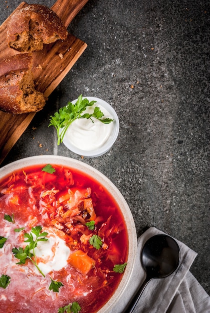 Soupe de légumes russe ukrainienne traditionnelle bortsch, à la crème dure. Petits pains de seigle persil, sur table en pierre noire, copie espace vue de dessus