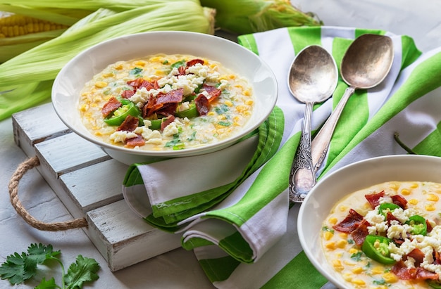 Soupe de maïs maison fraîche avec bacon, jalapeno et fromage de chèvre dans des bols sur béton gris clair