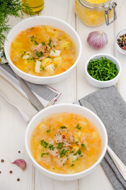 Soupe maison aux légumes, thon en conserve et grains de maïs dans un bol sur un bois blanc