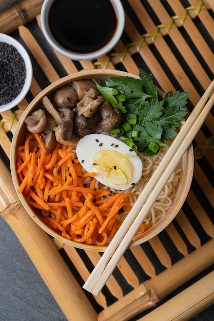 Soupe de nouilles ramen dans un bol blanc bol avec oeuf de poulet carottes champignons sur un plateau en bambou sur un fond de pierre sombre