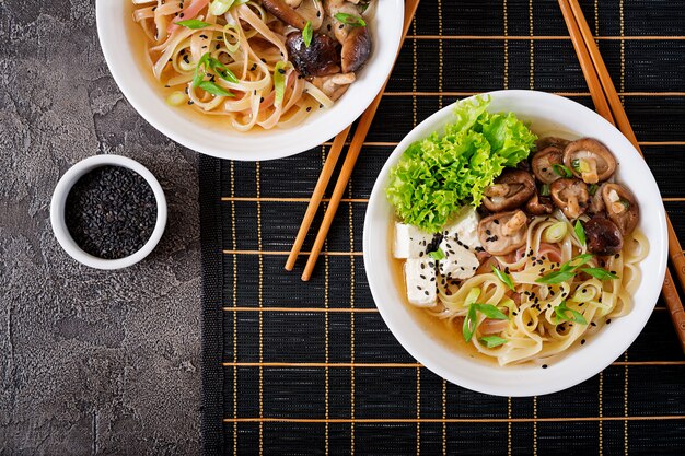 Soupe de nouilles végétaliennes avec du tofu, des champignons shiitake et de la laitue dans un bol blanc. Nourriture asiatique. Vue de dessus. Mise à plat