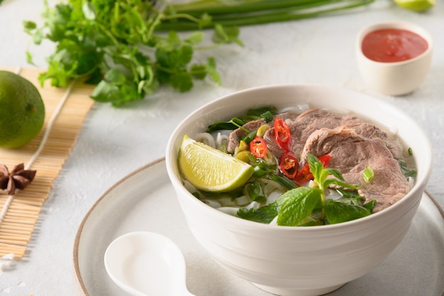 Soupe Pho bo au boeuf dans un bol blanc sur fond clair cuisine vietnamienne