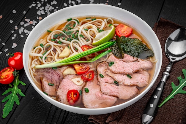 Soupe Pho Bo avec nouilles de riz boeuf gingembre citron vert piment dans un bol sur fond noir Cuisine vietnamienne et asiatique