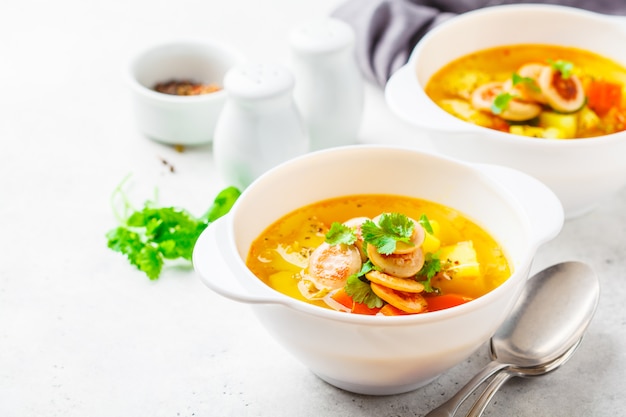 Soupe de pommes de terre allemande avec des saucisses et des légumes dans des bols blancs, fond blanc.