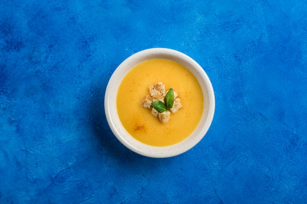 Soupe de potiron et carotte à la crème et aux épinards avec des craquelins sur un fond bleu classique.