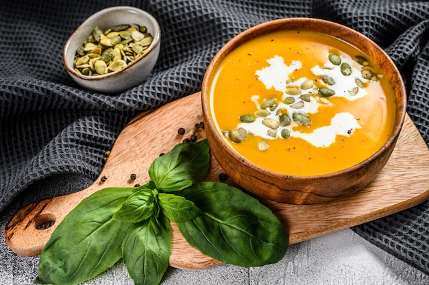 Soupe de potiron avec crème, graines et basilic frais dans un bol en bois rustique. fond gris. Vue de dessus