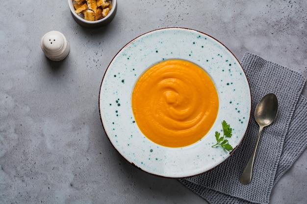 Soupe de potiron à la crème, des morceaux de pain et des noix de cèdre dans une plaque en céramique grise sur la surface de la table grise