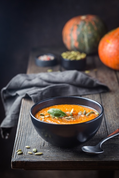 Soupe de potiron dans une assiette noire sur bois foncé. Décorations d'automne.