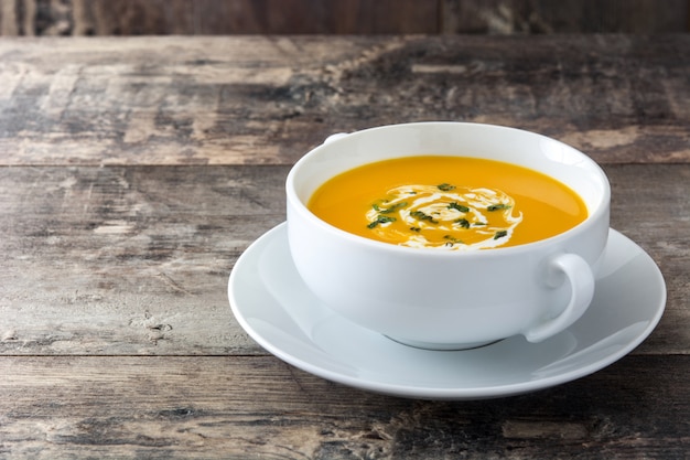 Soupe de potiron dans un bol blanc sur l'espace de copie de table en bois