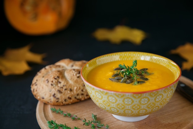 Soupe de potiron maison végétalienne d'automne en gros plan avec des graines, des herbes et du pain, sur fond noir