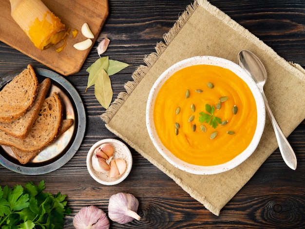 Soupe de potiron en purée dans une assiette blanche, graines de citrouille, pain, ail sur fond en bois foncé