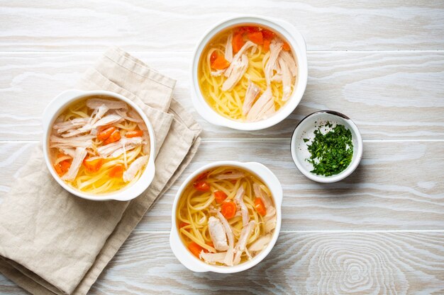 Soupe de poulet maison saine et chaude dans des bols en céramique blanche sur fond de table en bois blanc. Soupe traditionnelle au poulet savoureuse, excellente pour la santé et le système immunitaire. Vue de dessus