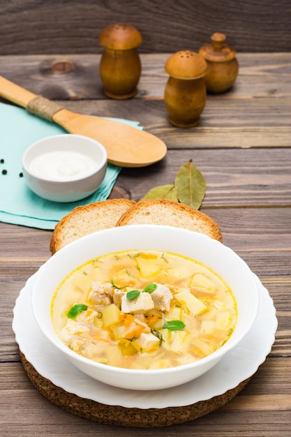 Soupe de poulet prête à manger avec pommes de terre et herbes dans un bol blanc sur une table en bois