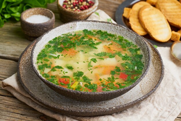 Soupe de poulet rustique avec garniture, persil, légumes, plat fait maison sur une vieille table sombre, vue latérale