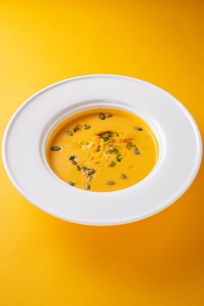 Soupe de purée de citrouille dans une assiette blanche sur fond jaune isolé