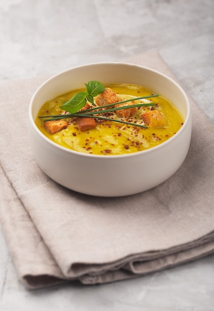 Soupe de purée de légumes bio avec craquelins, oignons verts et basilic sur une serviette en lin