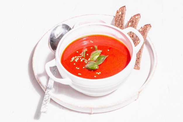 Photo soupe de purée rouge avec tomate, légumes verts et pain. lumière dure à la mode, ombre sombre. fond de mastic blanc, gros plan