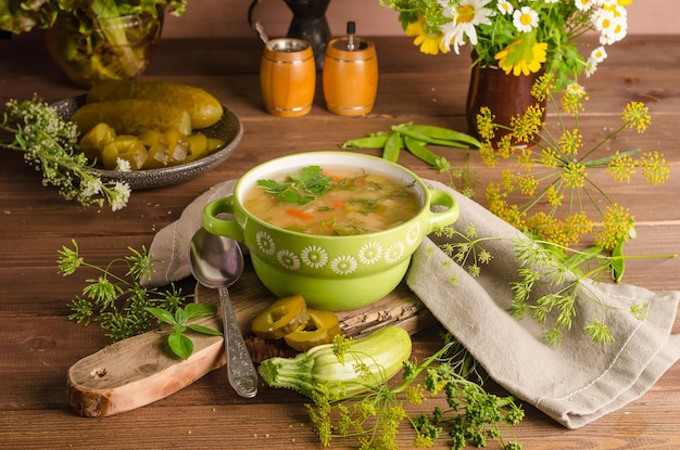 Soupe rassolnik traditionnelle avec cornichons marinés dans une soupière verte sur fond de bois