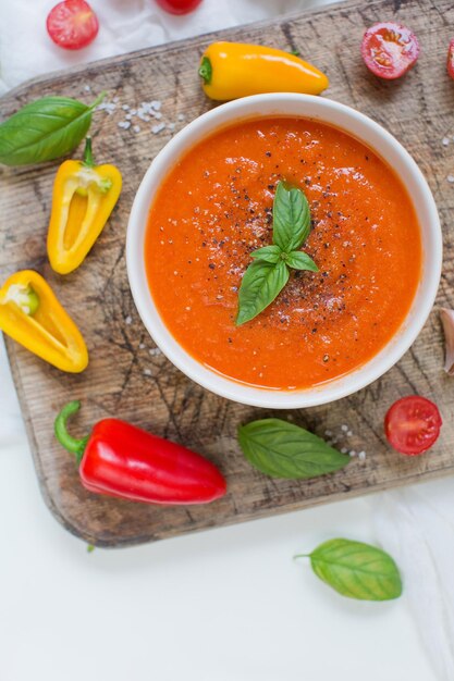 Soupe rouge végétalienne aux légumes avec tomates, poivrons, ail et basilic sur une planche à découper en bois