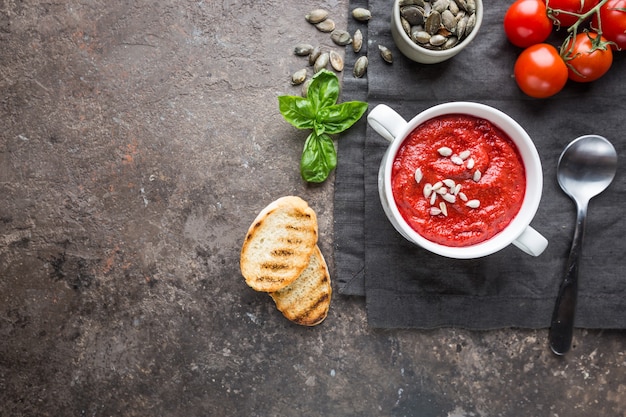 Soupe saine aux tomates dans un bol blanc avec des graines de crème et de tournesol, vue de dessus