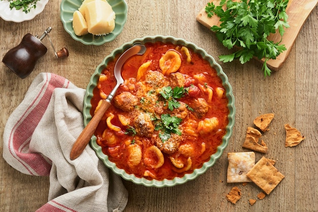 Soupe Soupe de tomates fraîches avec boulettes de viande, pâtes, légumes et persil dans un bol rustique vert sur fond en bois Cuisine italienne traditionnelle Dîner sain manger Vue de dessus Concept de dîner confortable d'automne