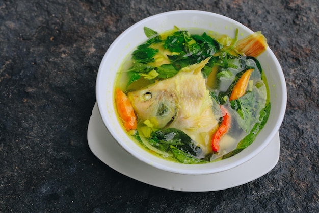 Soupe de tête de poisson Gurame ou sup kepala ikan gurame avec feuilles de basilic tomates curry jaune et piment dans un bol de nourriture indonésienne