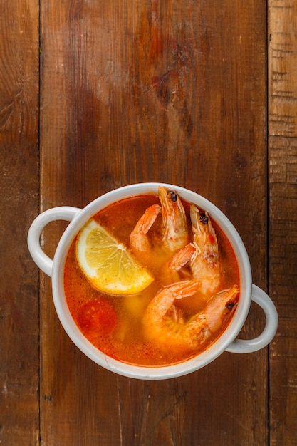 Soupe Tom Yam aux crevettes et lait de coco sur une table en bois. Photo verticale