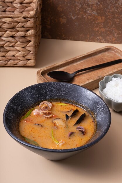 Soupe Tom yum avec des fruits de mer et du riz sur un fond beige