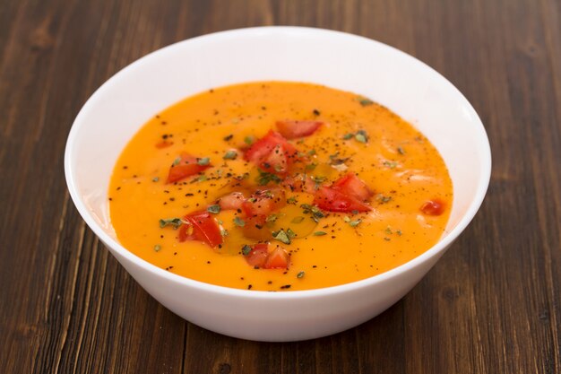 Soupe de tomate dans un bol blanc sur une surface en bois