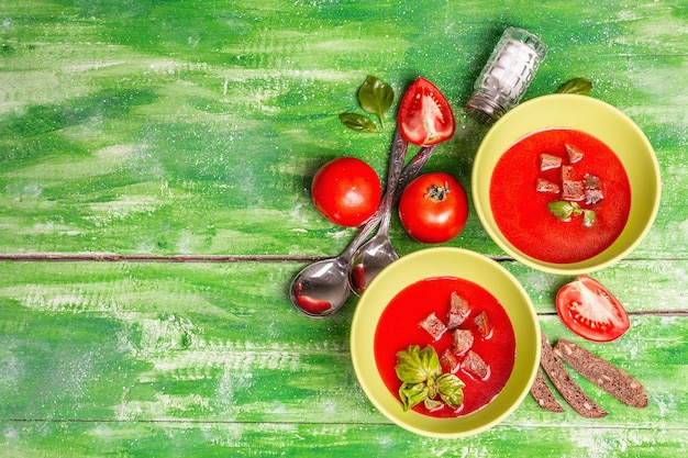 Soupe de tomates au basilic dans des bols. Légumes mûrs, légumes verts frais, épices parfumées. Table en bois