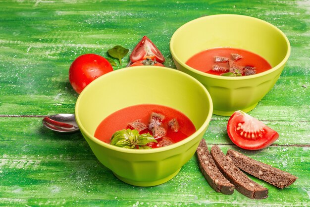 Soupe de tomates au basilic dans des bols. Légumes mûrs, légumes verts frais, épices parfumées. Table en bois