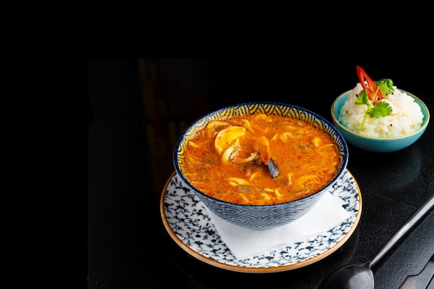 Photo soupe traditionnelle d'azian tom yam sur assiette sur fond noir copier l'espace