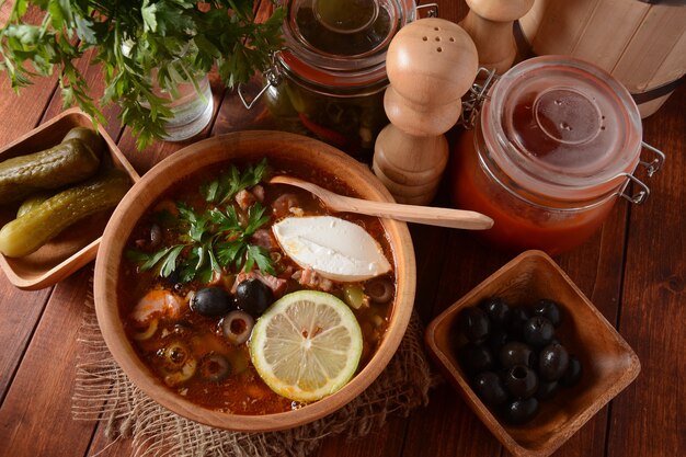 Soupe traditionnelle russe "Solyanka" avec de la viande, des saucisses, des concombres salés et des olives.Soupe dans un bol en bois de style rustique