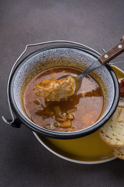 Soupe avec de la viande et des légumes dans un pot sur un fond sombre