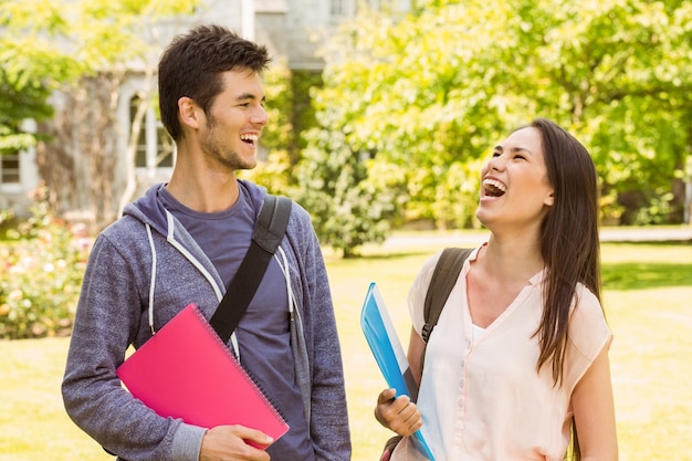 Souriant amis étudiant debout avec sac à bandoulière tenant le livre