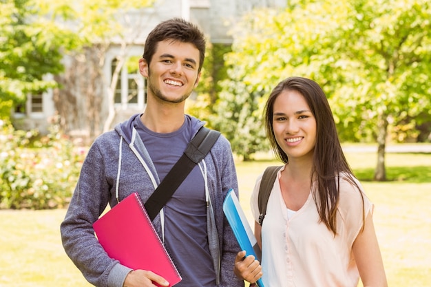 Souriant amis étudiant debout avec sac à bandoulière tenant le livre