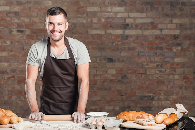 Souriant aplatissant la pâte avec un rouleau à pâtisserie sur le plan de travail de la cuisine