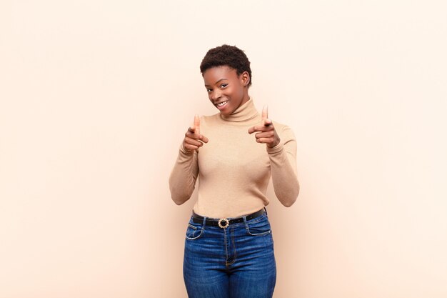 souriant avec une attitude positive, réussie et heureuse pointant vers la caméra, faisant signe de pistolet avec les mains