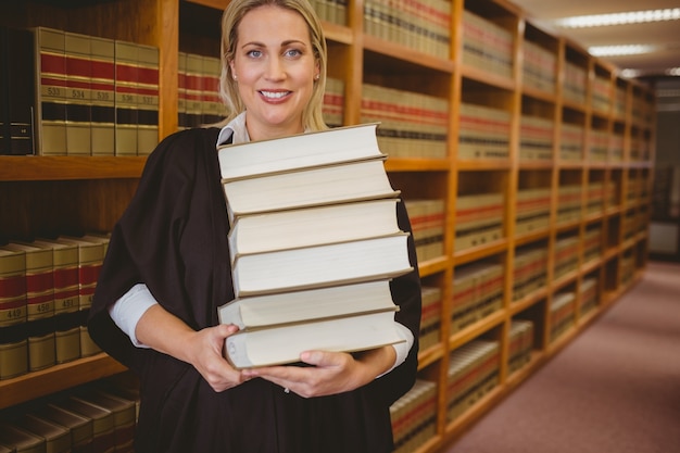 Souriant avocat tenant lourde pile de livres debout