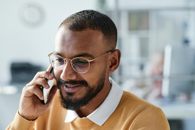 Souriant beau jeune chef d'entreprise métis avec barbe parlant au client par téléphone tout en travaillant au bureau
