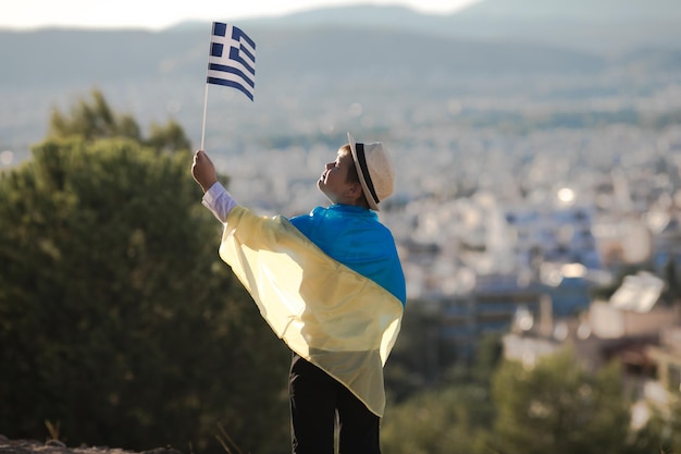 Souriant bébé garçon tenant un drapeau de la Grèce et de l'Ukraine sur fond de ville Pays d'amitié