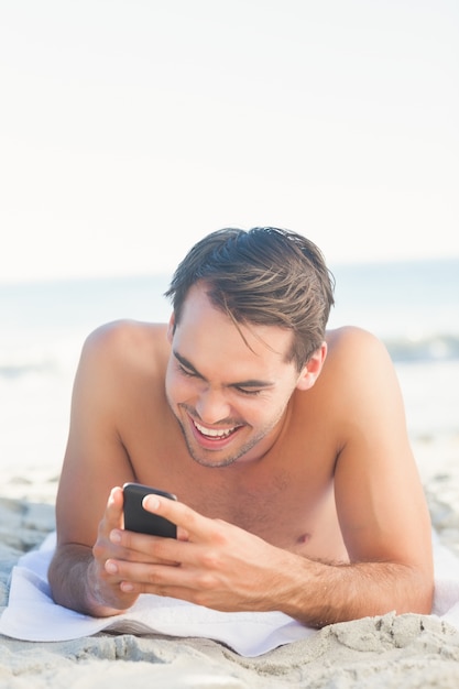 Souriant bel homme sur la plage en utilisant son téléphone portable