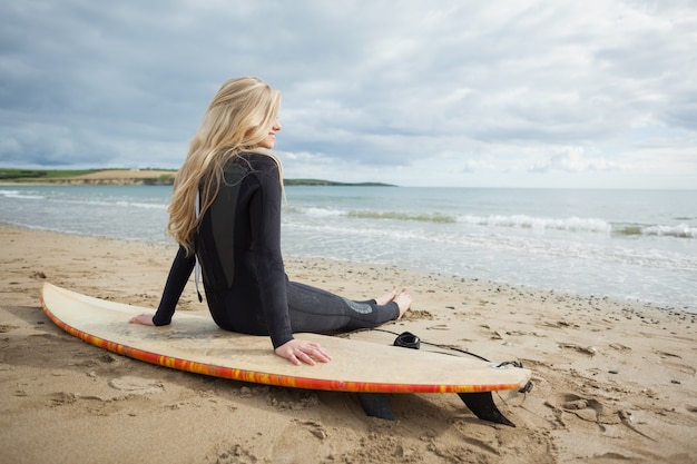 Souriant belle blonde en combinaison avec planche de surf à la plage