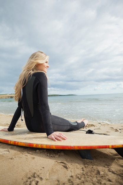 Souriant belle blonde en combinaison avec planche de surf à la plage