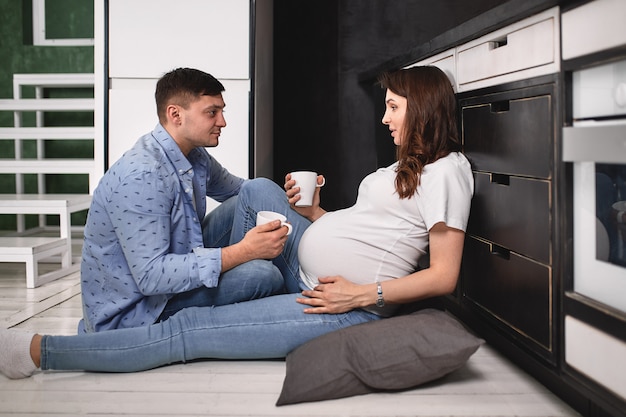 Souriant belle femme enceinte et homme dans la cuisine boire du café et cuisiner.