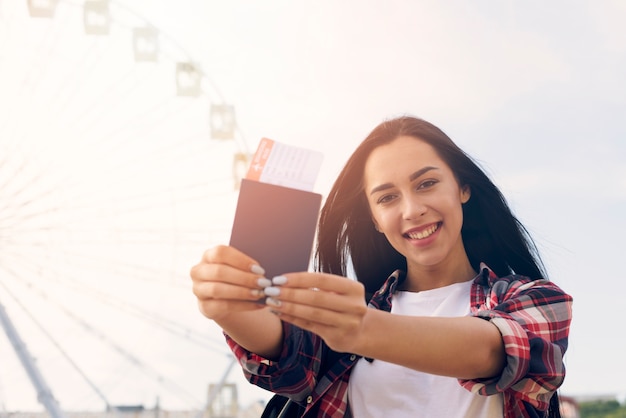 Souriant Belle Femme Montrant Un Passeport Et Un Billet D'avion Debout Près De La Grande Roue