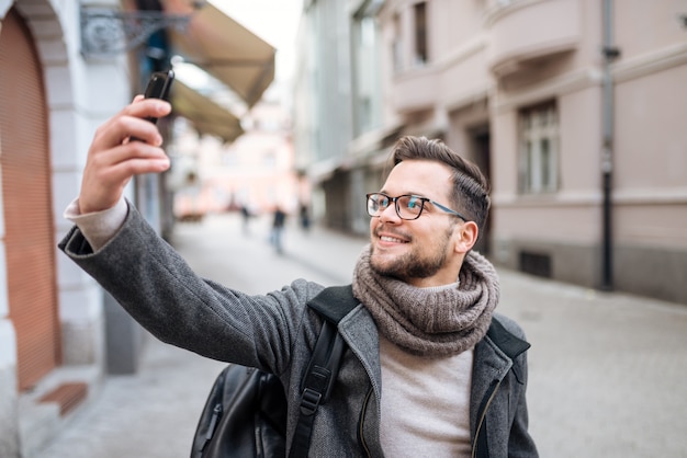 Souriant branché jeune homme prenant selfie dans la ville d&#39;hiver.