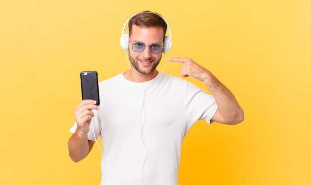 Souriant avec confiance, pointant vers son large sourire, écoutant de la musique avec des écouteurs et un smartphone