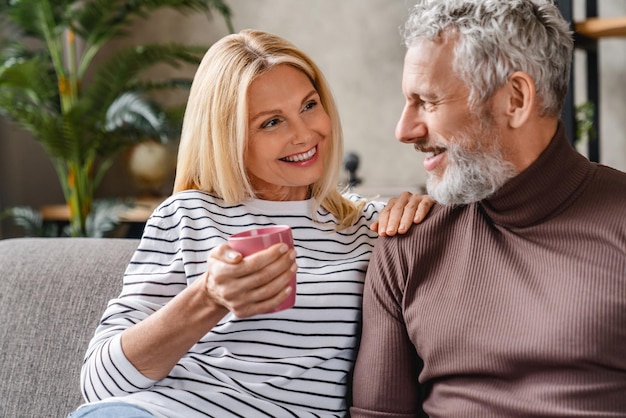 Souriant couple d'âge mûr d'âge moyen riant et buvant du café s'amusant à la maison