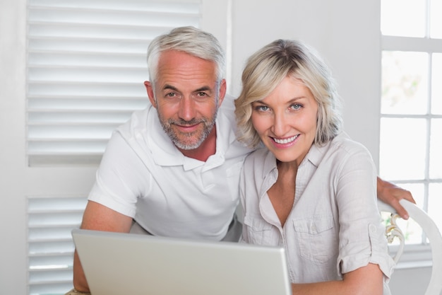 Souriant couple d&#39;âge mûr utilisant un ordinateur portable à la maison